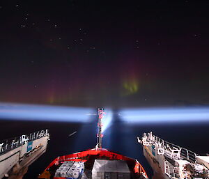 Looking out ofthe observation deck of the Nuyina in the night. The searchlight is panning around the and there is a purple green aurora visible