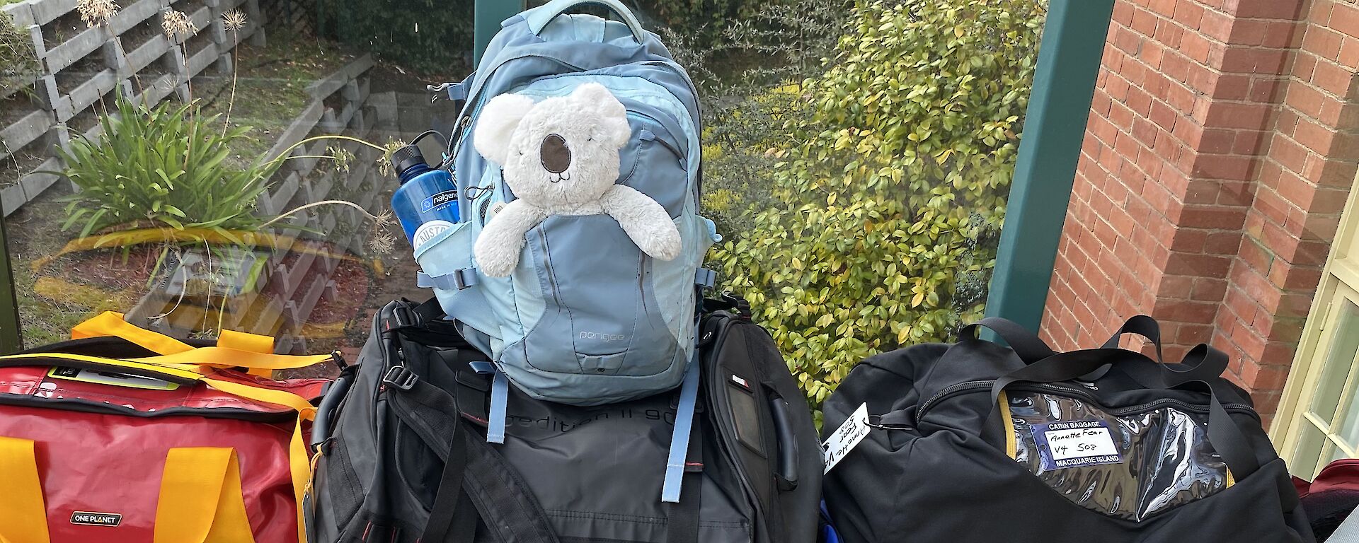 A selection of packed kit bags, with toy koala sticking out of front pocket of backpack on top of the pile