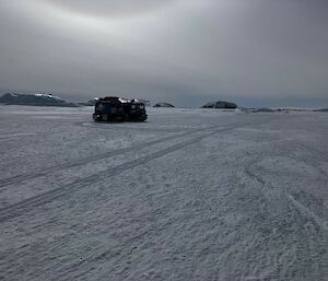 A blue snow tractor on the sea ice under a moody grey sky
