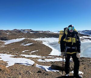A man on a hill with a rocky landscape, ice and a lake behind him