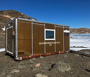 A brown shipping container, kitted out to be a shed, on a rocky hill