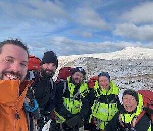 Five people stand on a snowy hillside