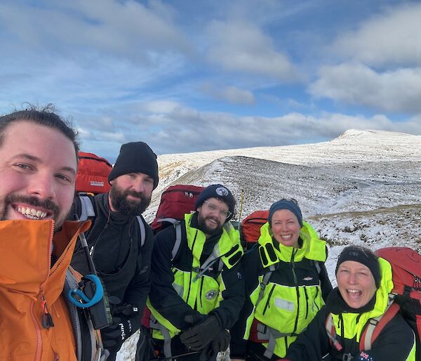 Five people stand on a snowy hillside