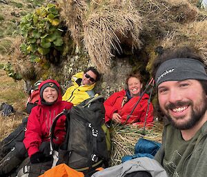 Four smiling people having a rest on brown tussock grass