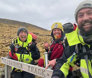 Three smiling people on a hillside with a sign saying Tiobung Track