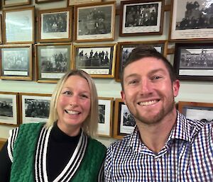 A blonde smiling woman in a green woollen vest sits with a smiling man in a blue check shirt