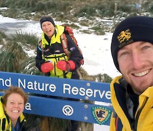 A man and two women with snow around, near the Macquarie Island Nature Reserve sign