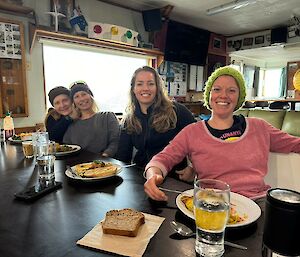 Four women sit at a bar with food and drinks near them