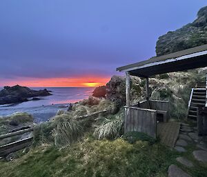sun rising over the sea with a field hut to the right and beach to the left