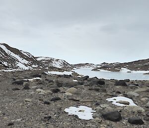 A rocky valley with hills each side, covered in snow, and people walking along.