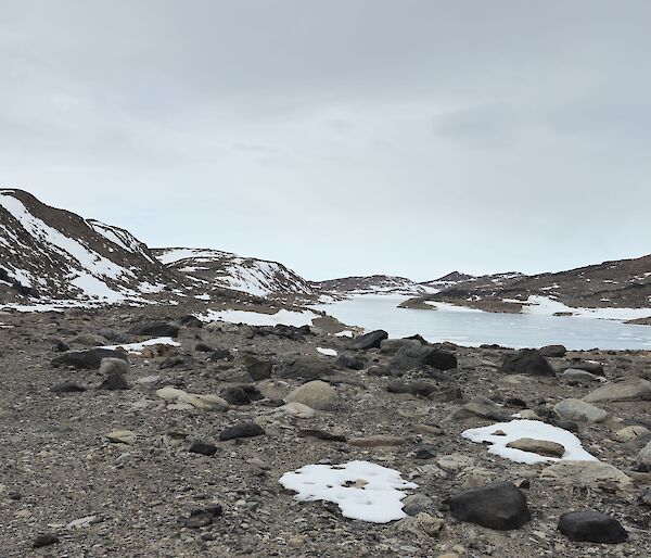 A rocky valley with hills each side, covered in snow, and people walking along.
