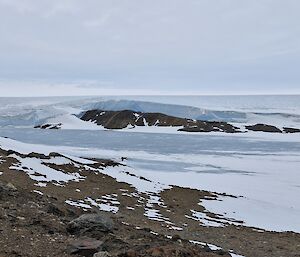 Taken from a hill, looking out on a snowy expanse with rocky hills in the middle.