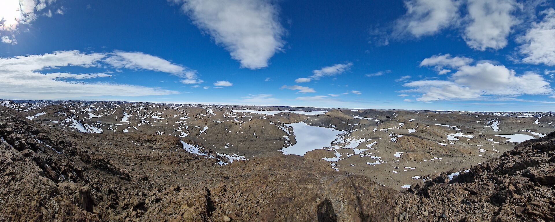 A rocky plain with bits of snow here and there under a blue sky
