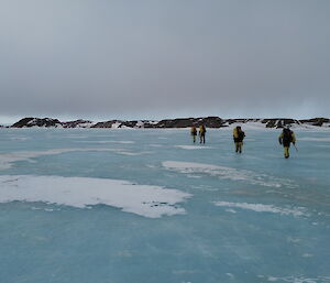Five people walk across an aqua-coloured frozen lake