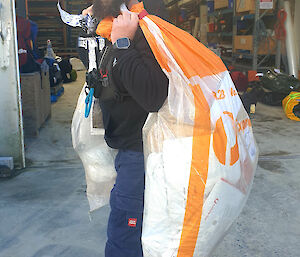 Man smiles at camera, holding two mailbags over shoulders