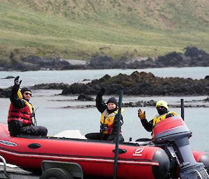 Inflatable rubber boat on trailer being pulled from water, three crew waving to camera