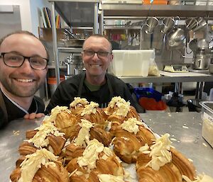 Two chefs in black near a tray of almond croissants