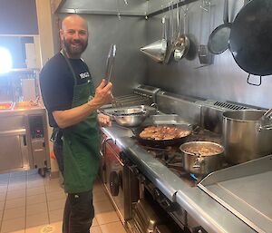 A man stands in a commercial kitchen wearing a green apron.