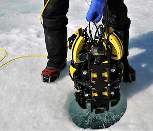 A small submersible instrument being lowered by hand through a hole in ice.