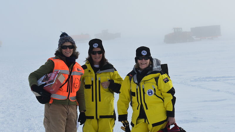 Three women in yellow Antarctic gear standing on a snowy slope