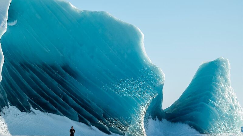 A person with a massive green iceberg behind them
