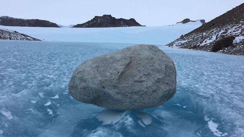A grey boulder sits on frozen icy waves