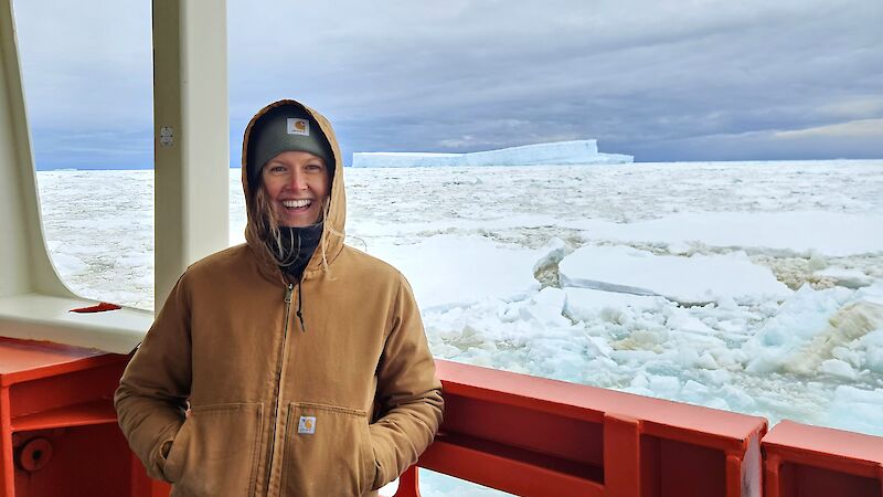 A smiling woman in a hoody stands on the deck of an icebreaker