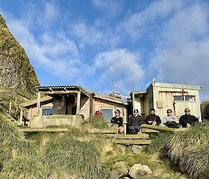 A brown and cream hut with five people sitting out front