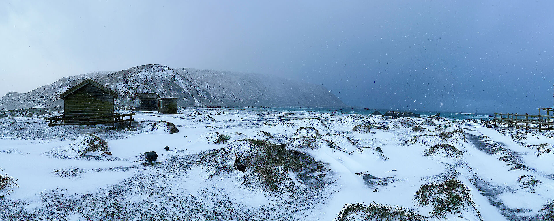 A snowy slope with a field hut on the left and ominous grey cloud ahead