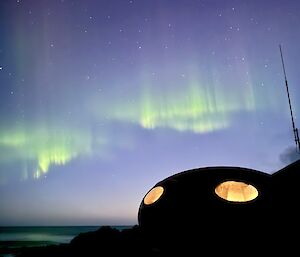 A round melon hut at night time with lights on inside, and an aurora above