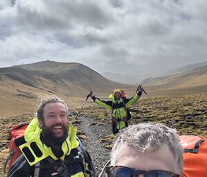 Three smiling people on a bike - treeless plateau behind them and clouds