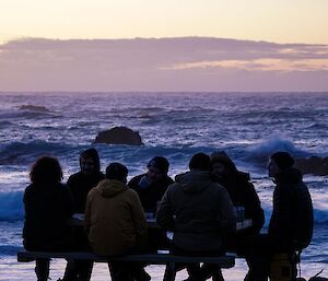 A group of people sit in shadow in front of a raging beach