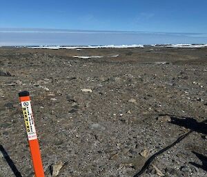 An orange guide post in flat, rocky ground, with sea ice in the distance