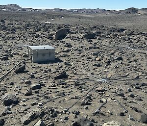 A star shaped array of cables running across grey, rocky ground and attached to a large silver metal box.