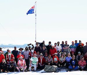 group of around 50 people wearing Christmas clothing outside on snow and ice with a flag in the background