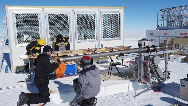Four scientists setting up ice-drilling equipment, surrounded by snow and ice