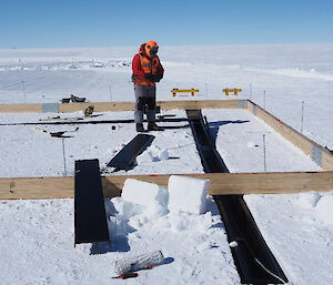 A man standing inside a wooden frame in the snow.