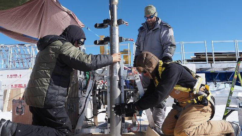 Three people guiding the ice-drill into the ice