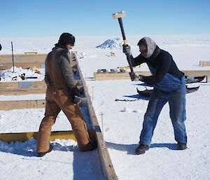 One person holding a hammer while another person secures a wooden frame