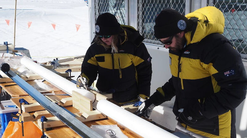 Two people standing beside an ice core lying on a table in the field.