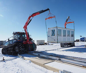 A tractor cranes a white shipping container into position in the drill shelter site.