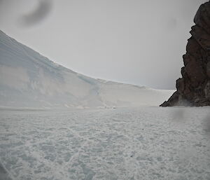 A frozen body of water with a large ice wall on the left and a large rock face on the right, forming a natural amphitheatre.