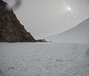 A frozen body of water with a large ice wall on the right and a large rock face on the left, forming a natural amphitheatre.