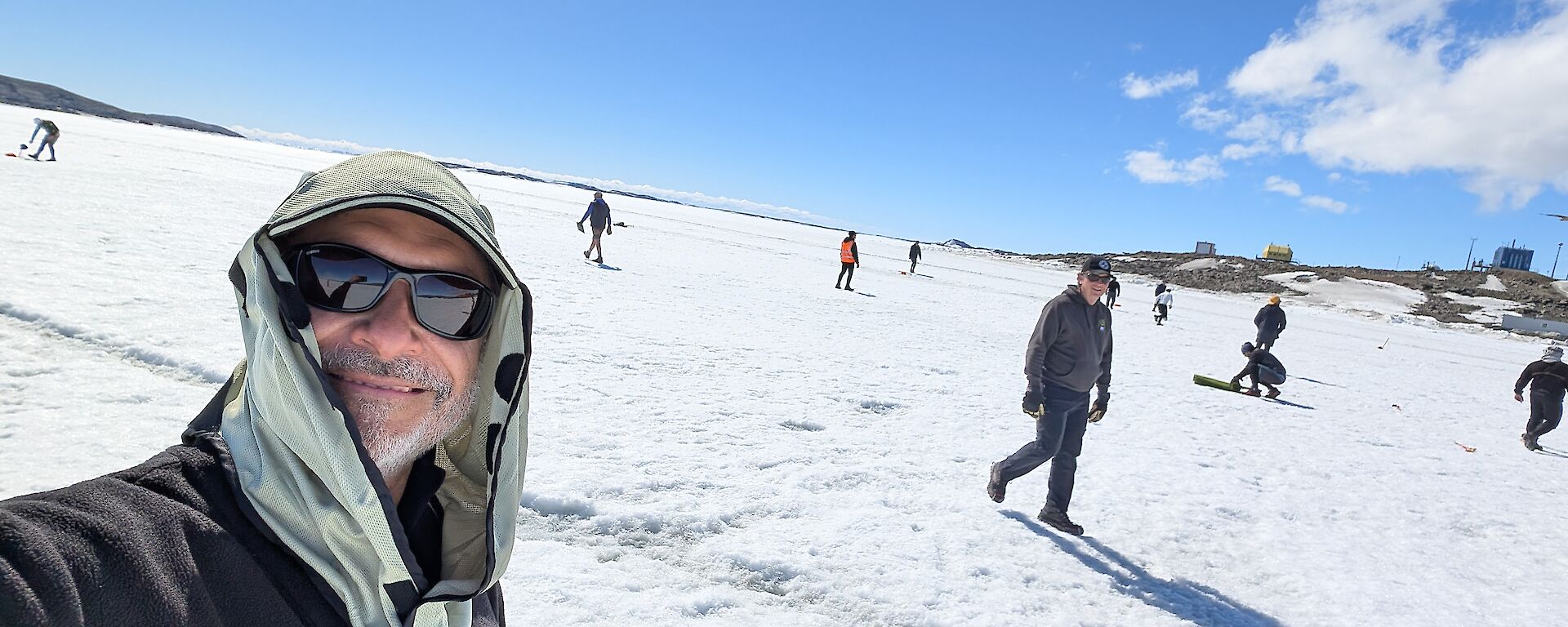 Louis takes a selfie on the sea ice out front of Davis station. There's numerous expeditioners setting up to play a game of cricket on the ice.