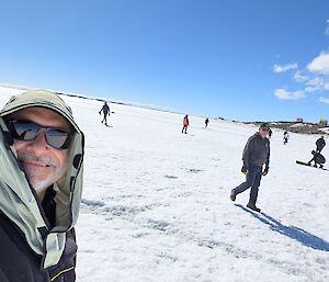 Louis takes a selfie on the sea ice out front of Davis station. There's numerous expeditioners setting up to play a game of cricket on the ice.