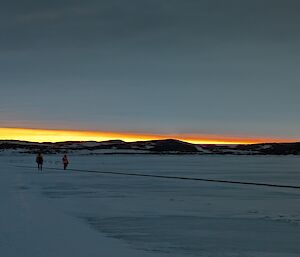 Louis and another expeditioner are walking along the sea ice inspecting the fuel line that connects from RSV Nuyina to Davis Station..
