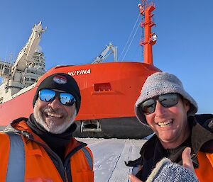 A selfie of Louis and Brendan standing on the sea ice with RSV Nuyina behind them.