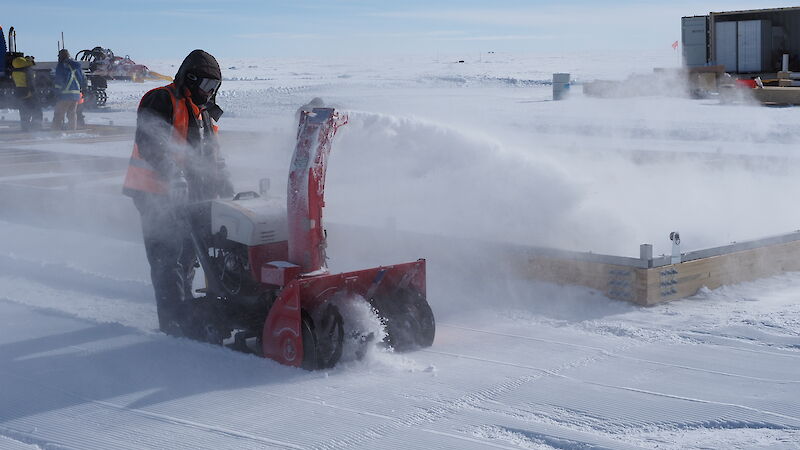 A man using a snow blower to blow snow in to a wooden frame
