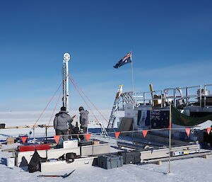 Two people standing beside an ice core drill, surrounded by drilling equipment.