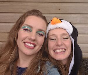 A woman wearing eye make-up and a woman dressed as a penguin